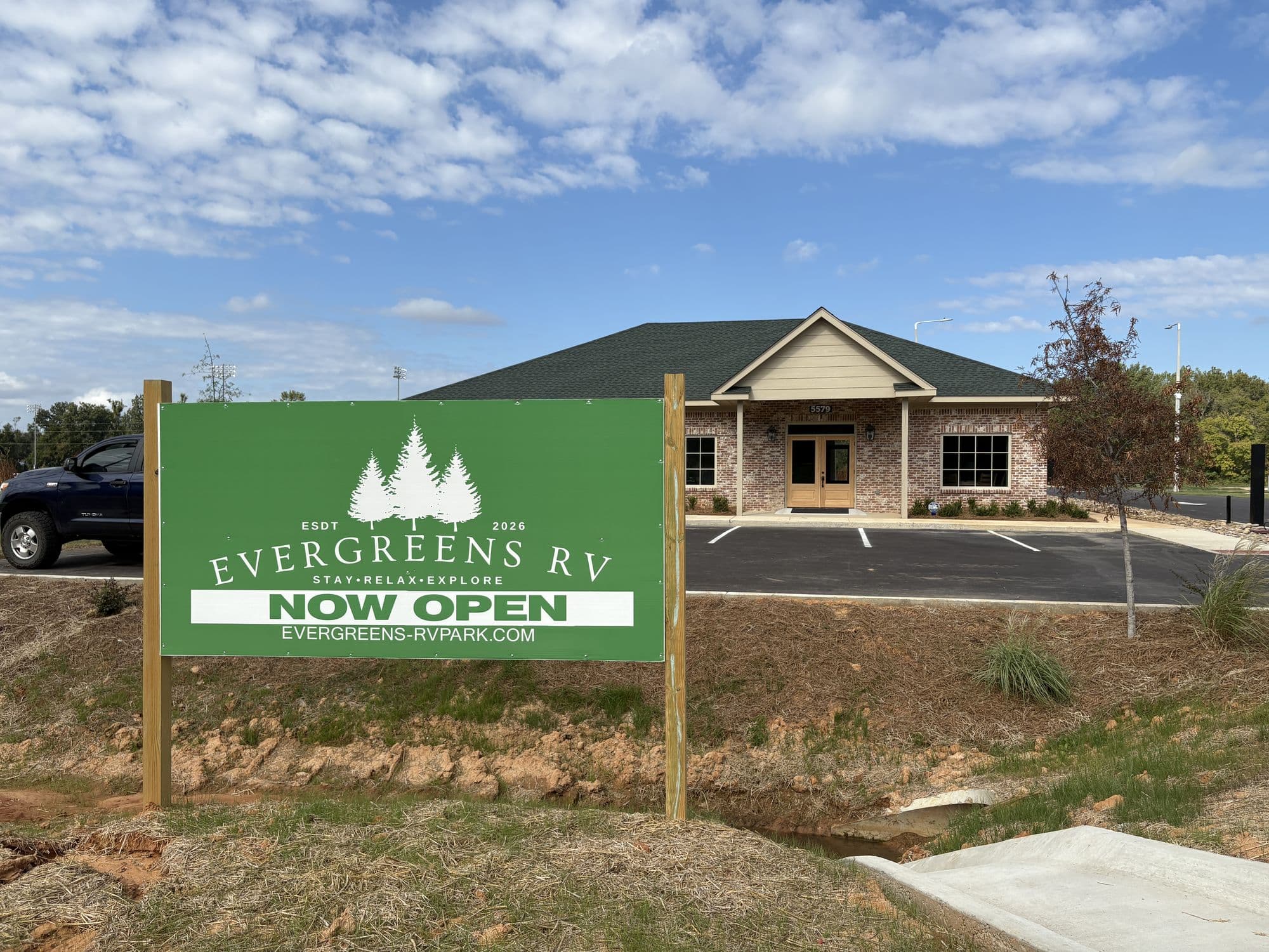 The green Evergreens RV Now Open sign at the entrance, with the park office behind it