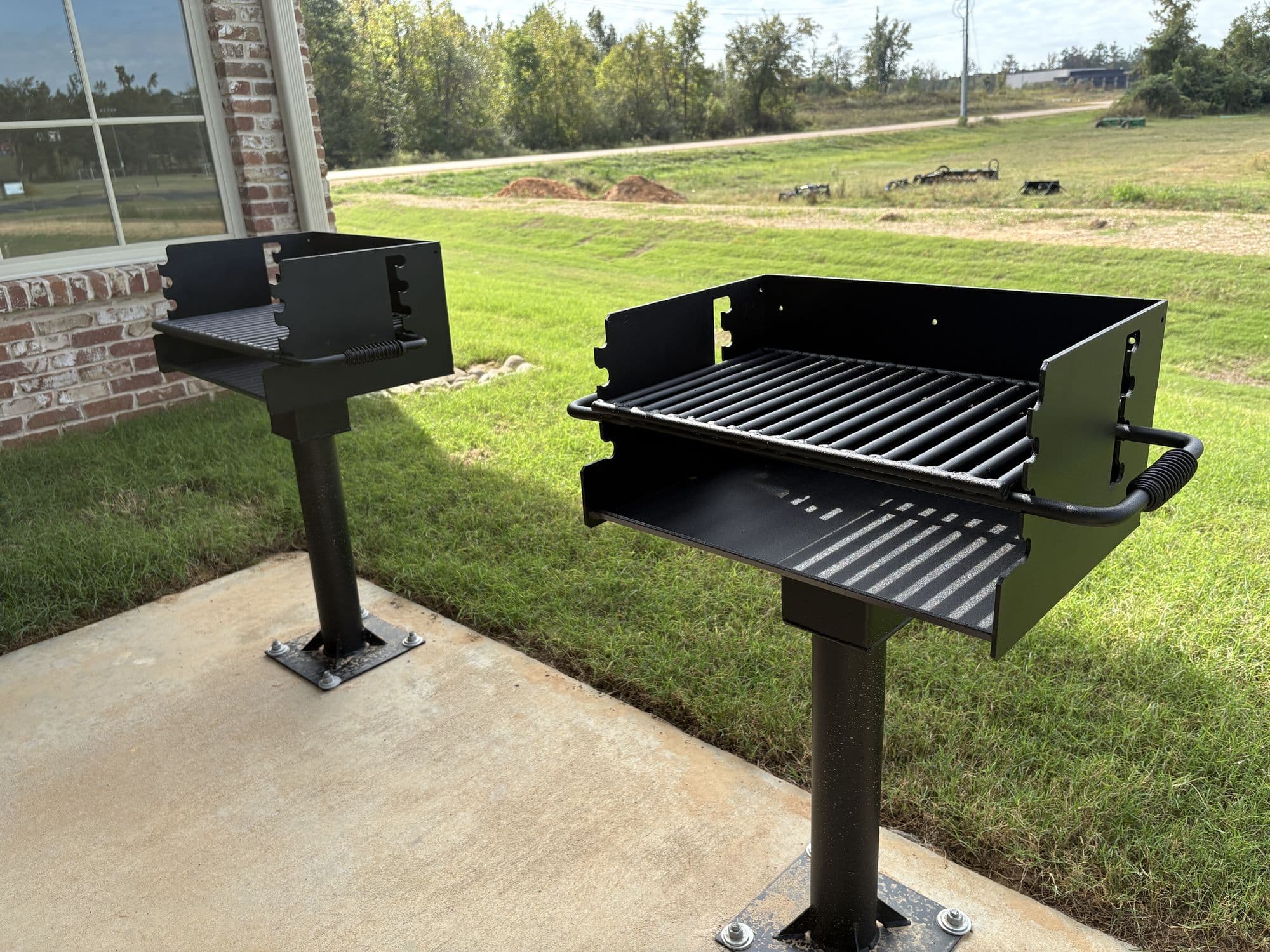 Two pedestal charcoal grills on a concrete pad beside the pavilion